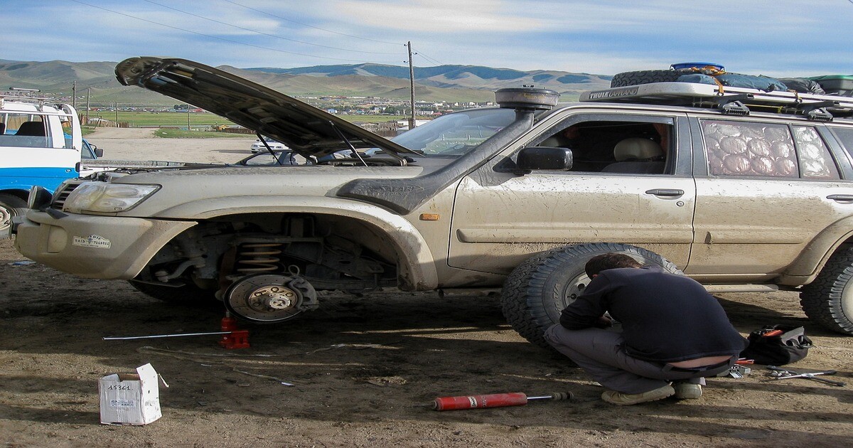 A man fixing a tyre with the car shock absorbers clearly visible. 