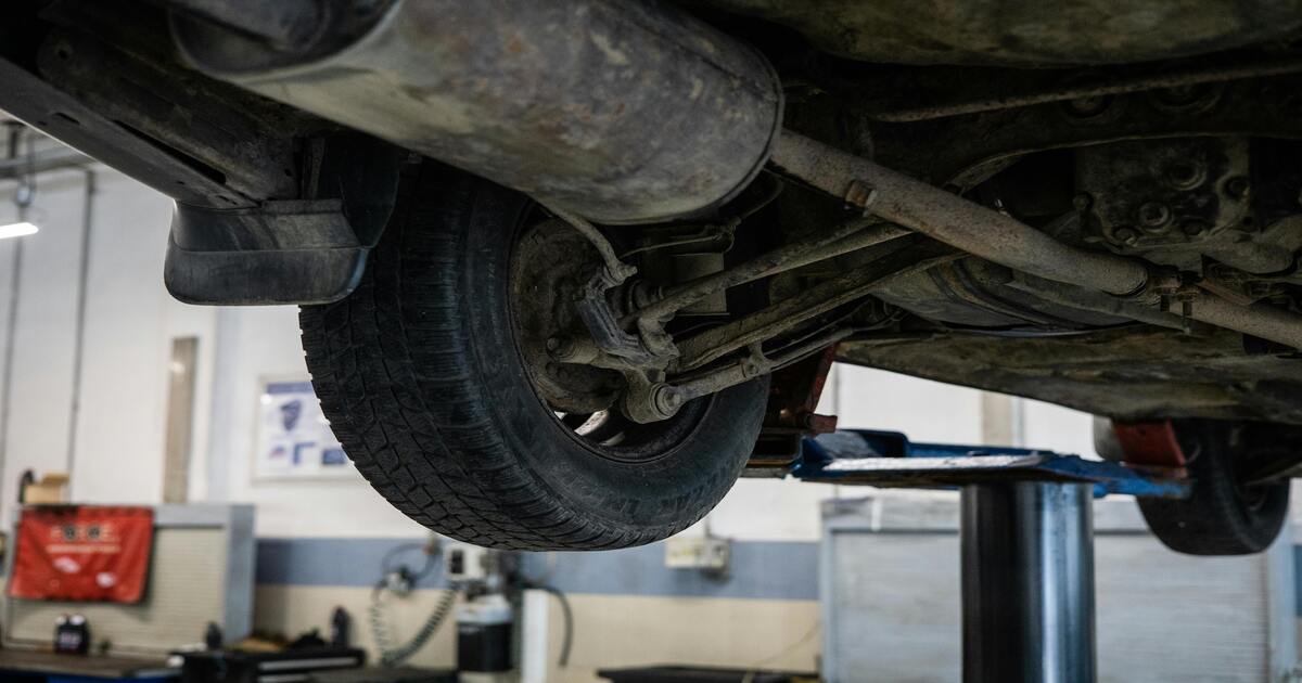 The undercarriage and exhaust system of a dirty car in a car shop.