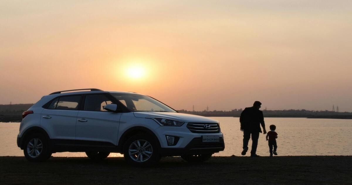 A man and a child in front of a white SUV at sunset.