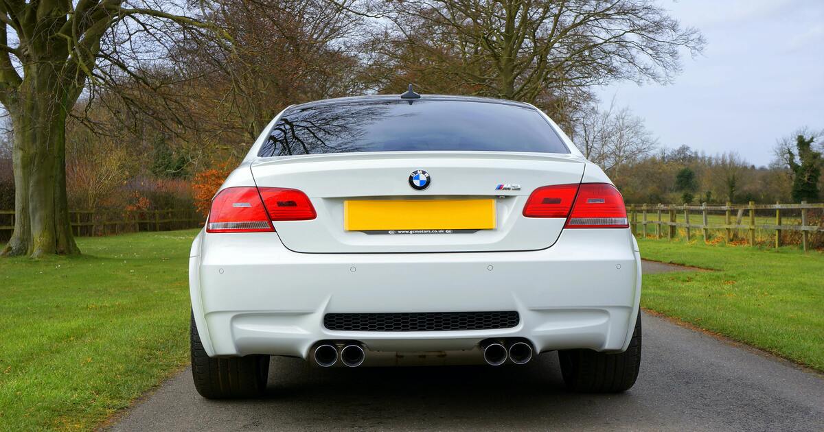 A white car with mufflers parked near trees. 